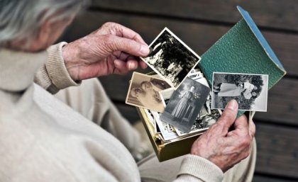 Elderly woman holding old photographs. Adobe.